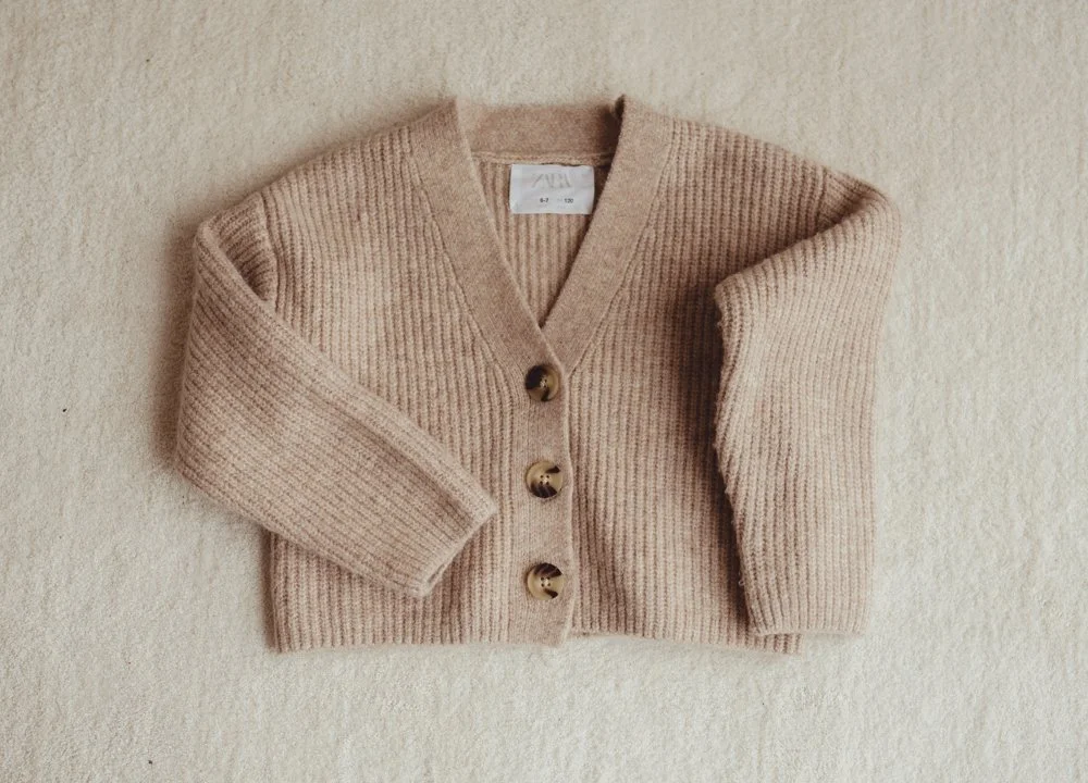 A folded beige knit cardigan with large buttons on a cream surface.