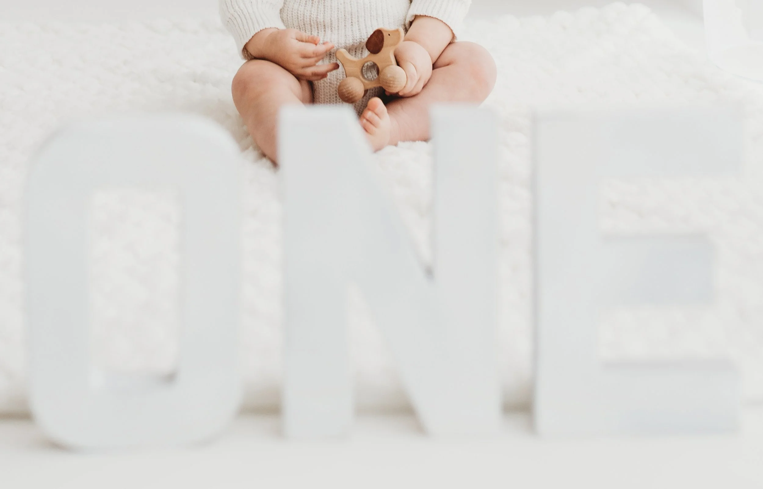 A baby sitting on a white blanket holding a small wooden toy dog with wheels.