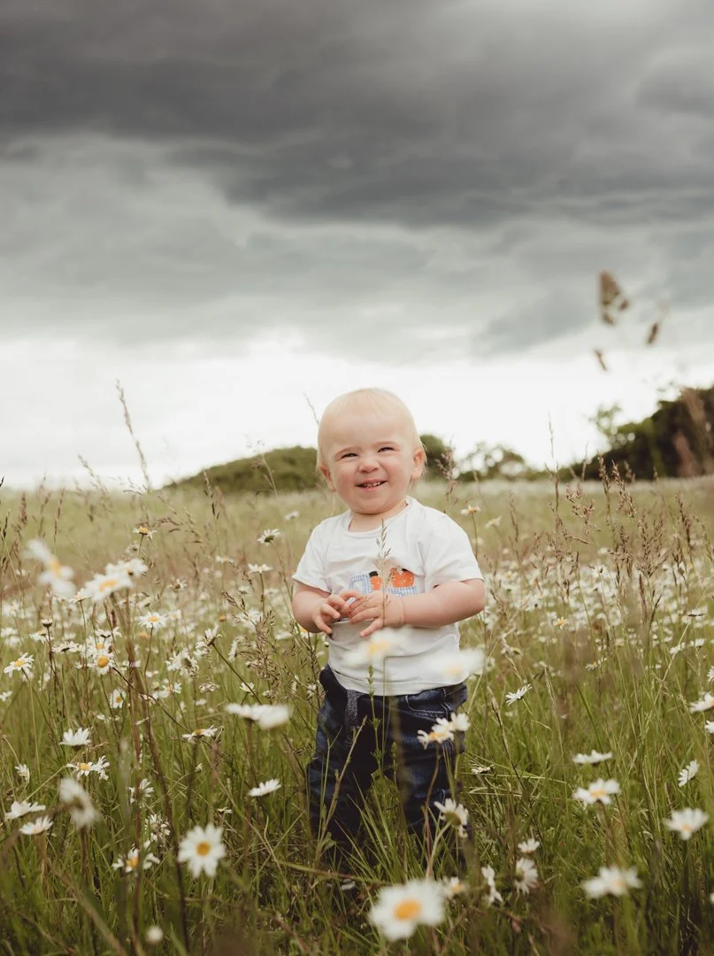 young child walking in a day meadow with stormy clouds above captured during a natural outdoor photoshoot in Saffron Walden Essex