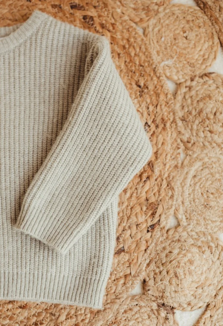 Close-up of a beige knitted sweater on a woven jute rug.
