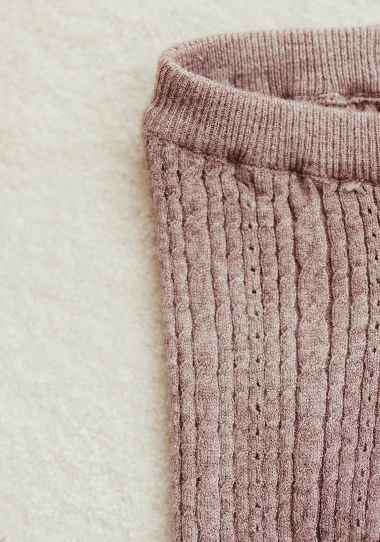 Close-up of a pink knit fabric with a ribbed texture, showing the top part of a sock or sleeve against a light background.