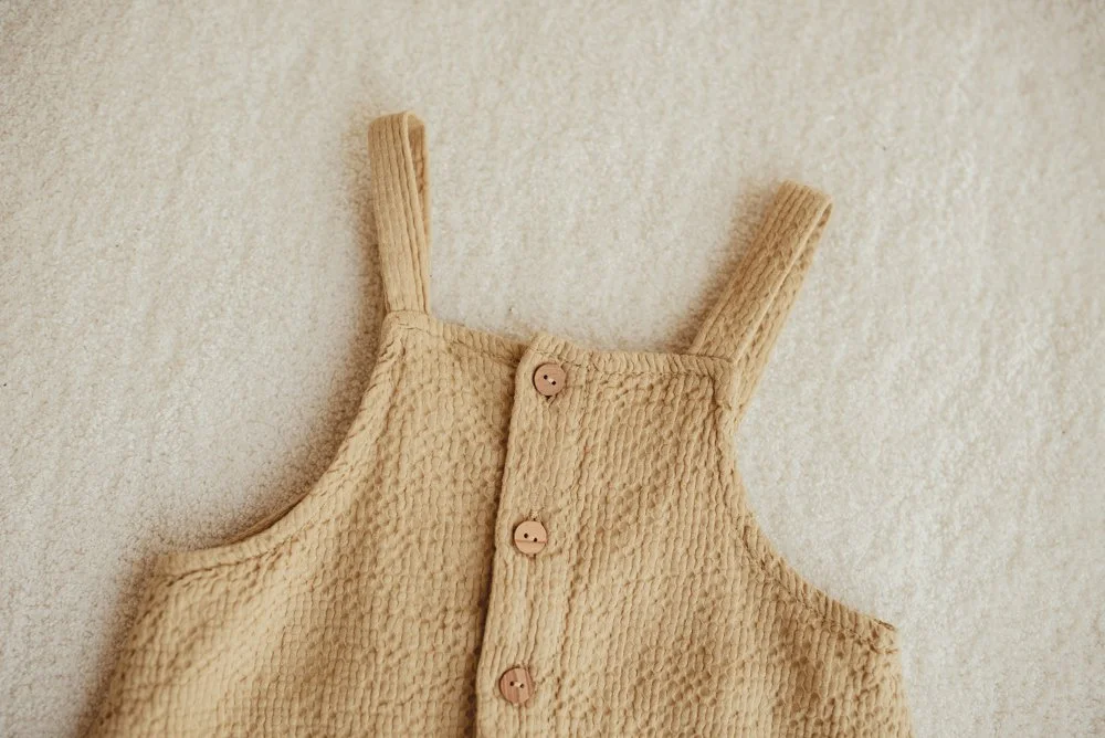 A beige textured sleeveless top with buttons on the front, laid flat on a soft, neutral background.