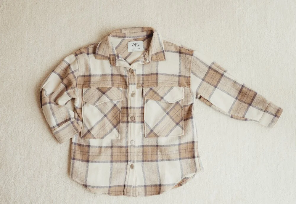 A long-sleeve plaid button-up shirt with two chest pockets, laid flat on a beige surface.
