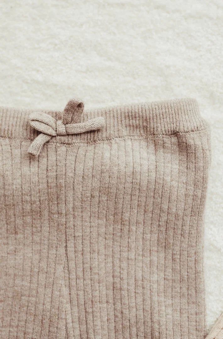 Close-up of a beige, ribbed, knit sweatpant with a drawstring tied in a bow at the waistband.