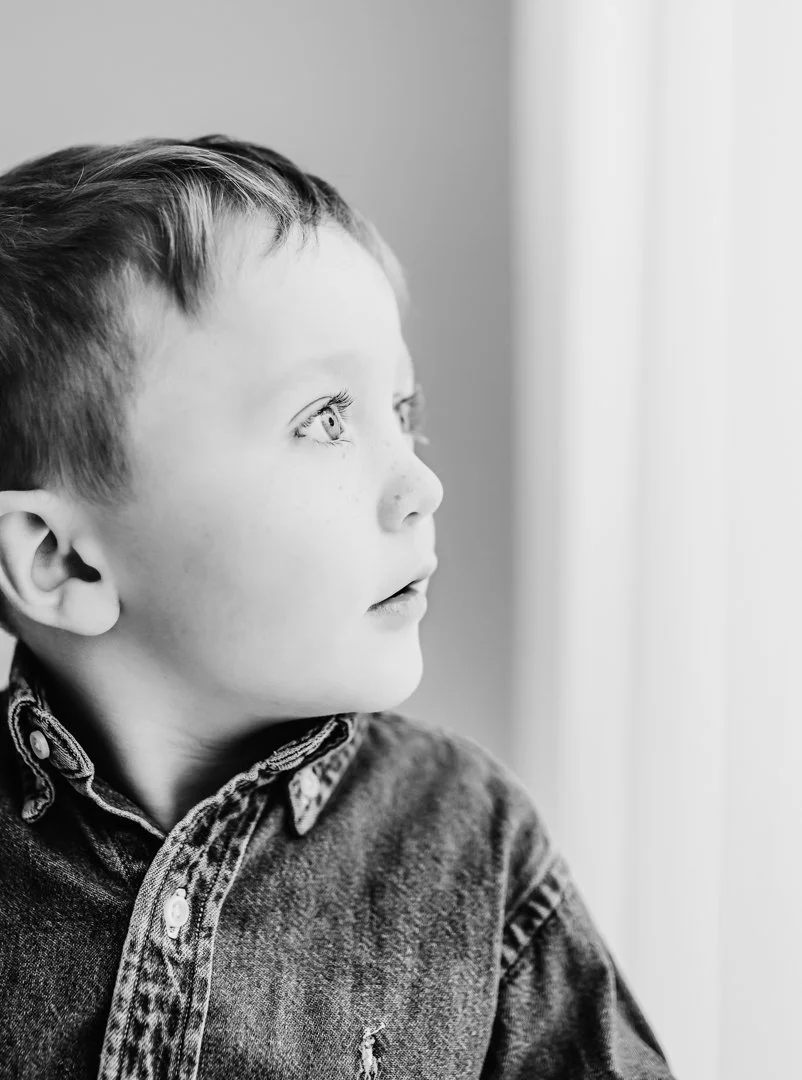 A young boy with light-colored eyes and short hair looking out a window.