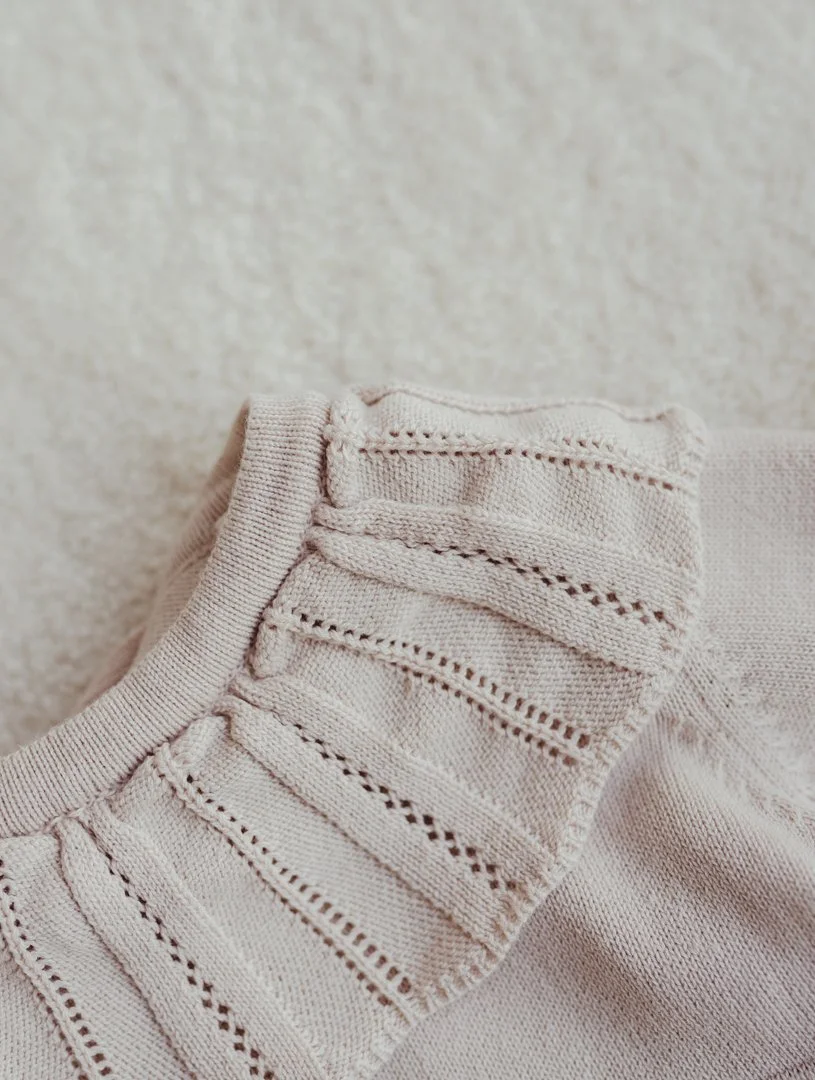 Close-up of a cream-colored knit sweater with a detailed pattern, lying on a soft, textured surface.