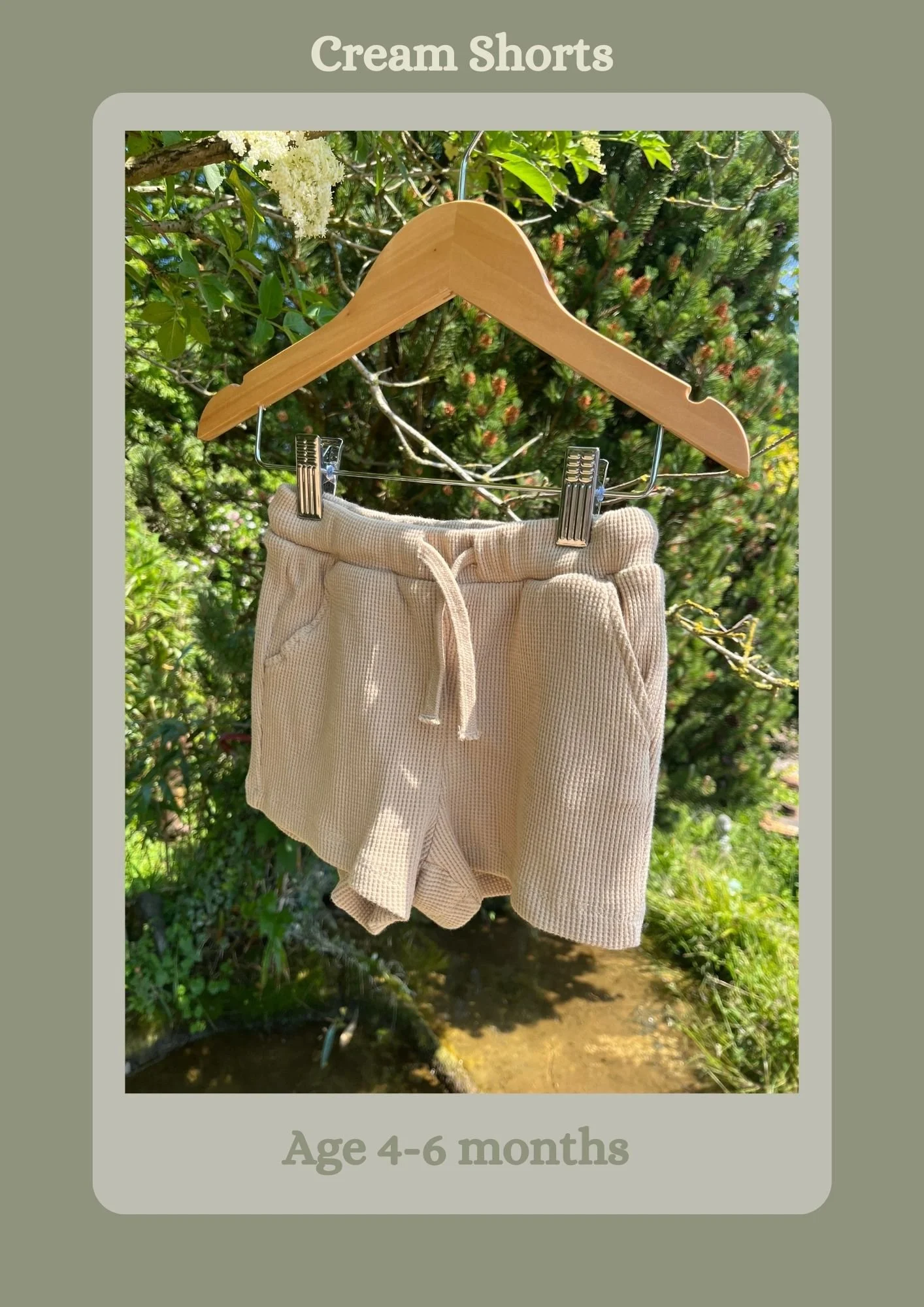 A pair of cream-colored shorts hanging on a wooden hanger outdoors, with green foliage in the background. The text indicates they are suitable for children aged 4-6 months and labeled "Cream Shorts" at the top.
