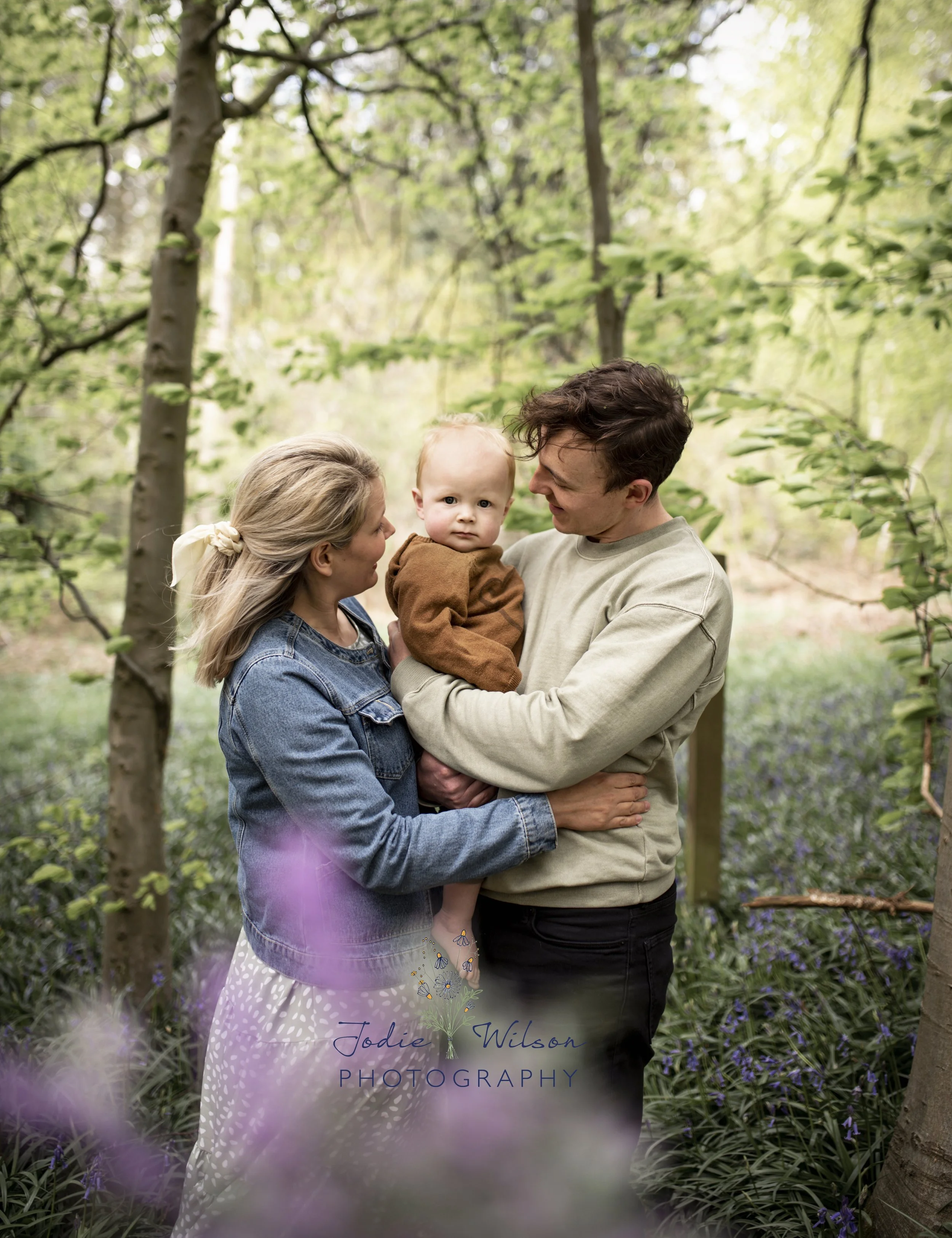 Relaxed family photoshoot in woodland filled with beautiful bluebells. Mum, Dad and baby