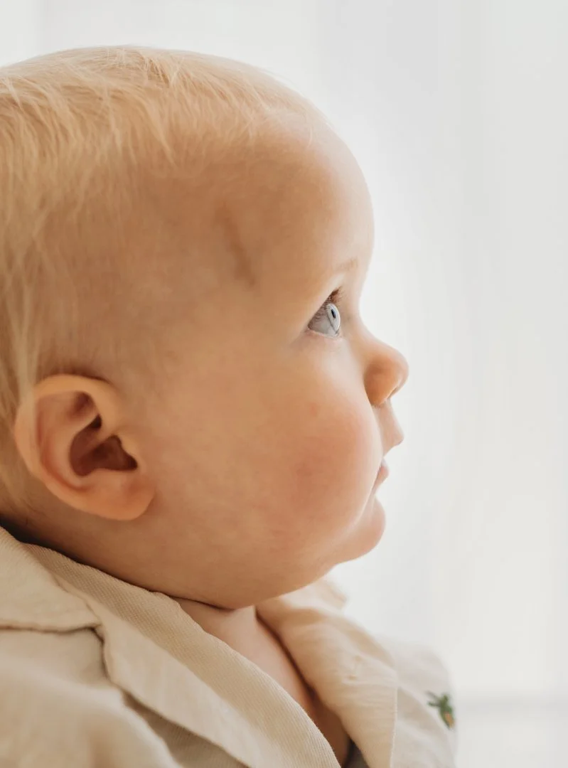 Profile of a young child with blonde hair and light skin, looking to the right, wearing a beige shirt.