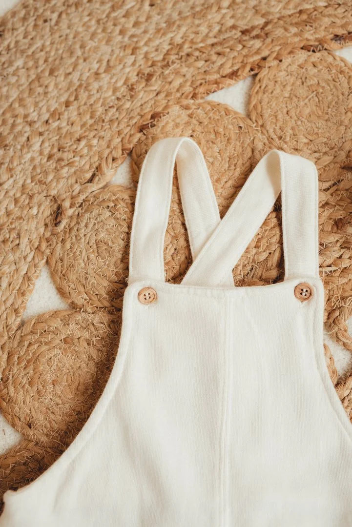 Close-up of a cream-colored knit baby romper with wooden button details, placed on a woven straw placemat.