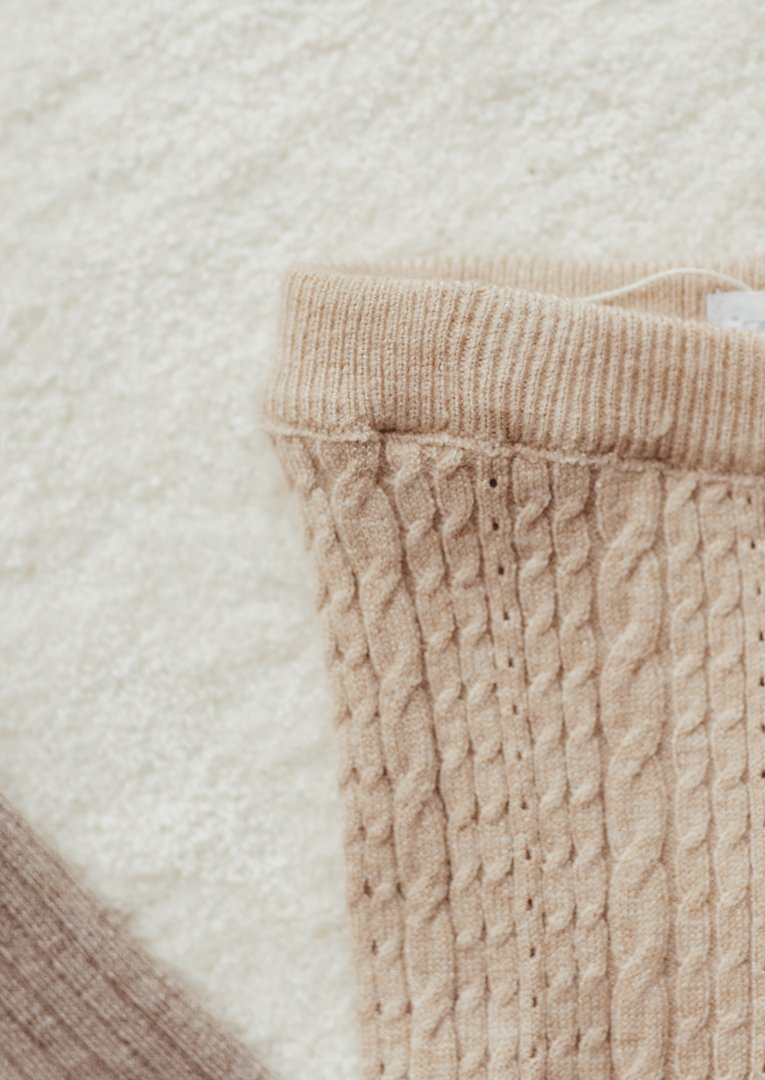 Close-up of a beige knitted sweater with a prominent cable knit pattern and ribbed collar.