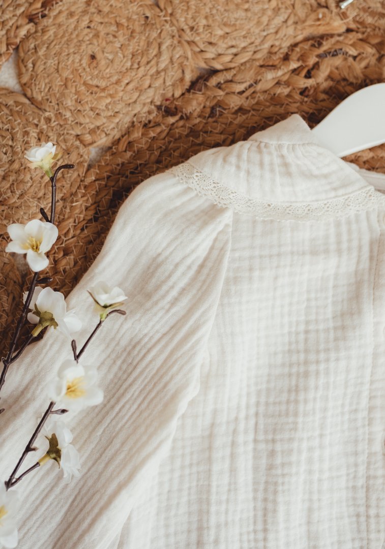 A wicker basket with white flowers, a white piece of fabric or clothing with lace, and a white object, possibly a plastic spatula or scoop.