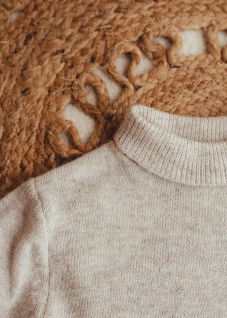 Close-up of a light-colored sweater next to a textured woven rug.