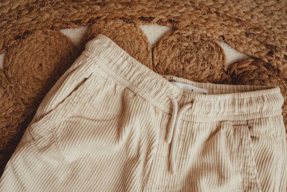 Beige ribbed pants with a drawstring lying on a woven straw surface.