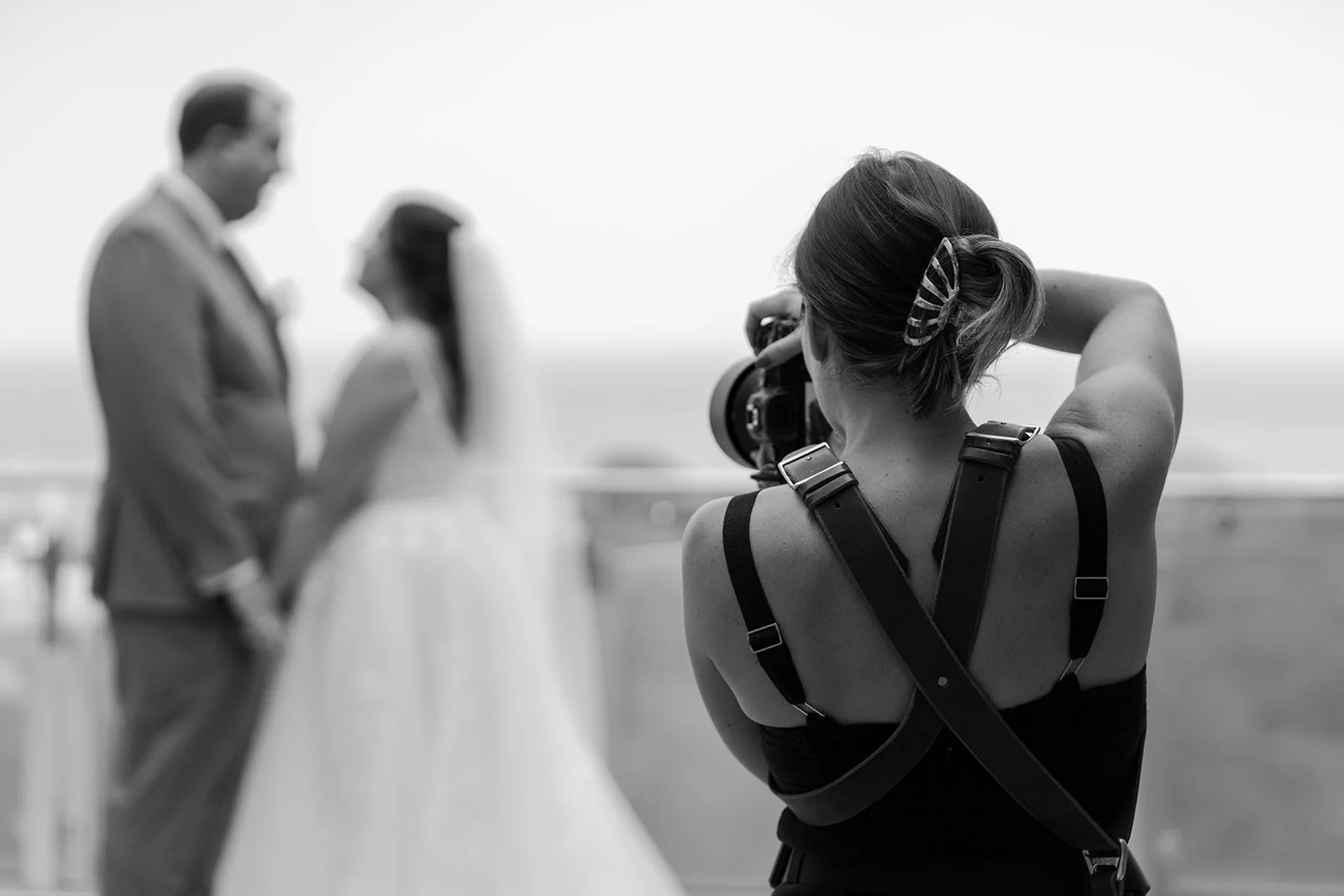 Photographer taking a black and white photo of a couple at the beach with blurred background.