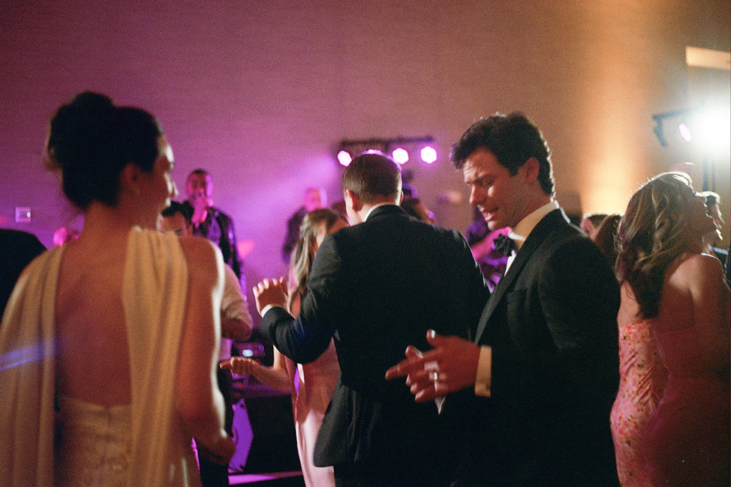 People dancing and socializing at a formal event with colorful lighting.