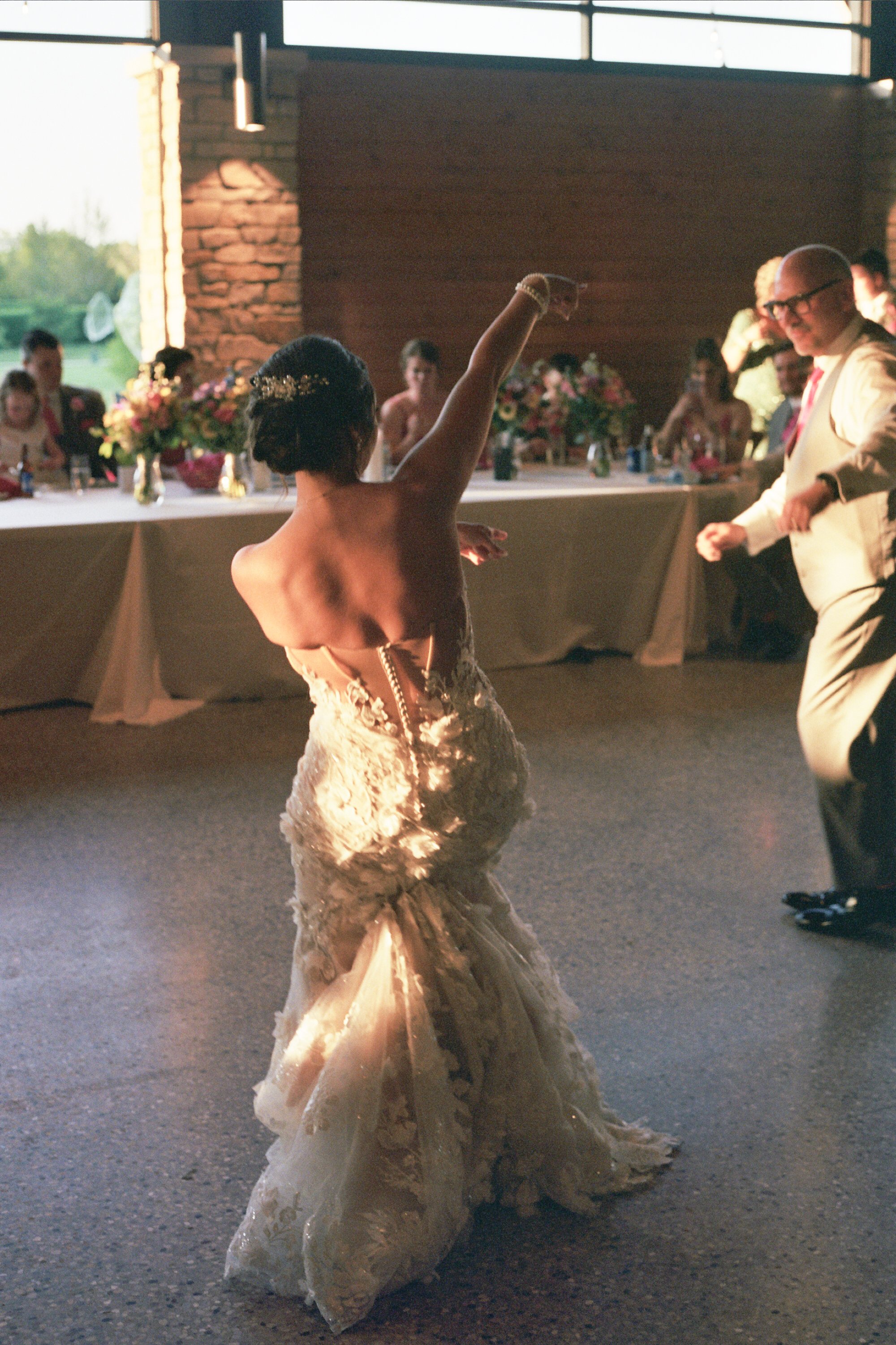 Bride dancing at wedding reception with guests seated at decorated table in the background.