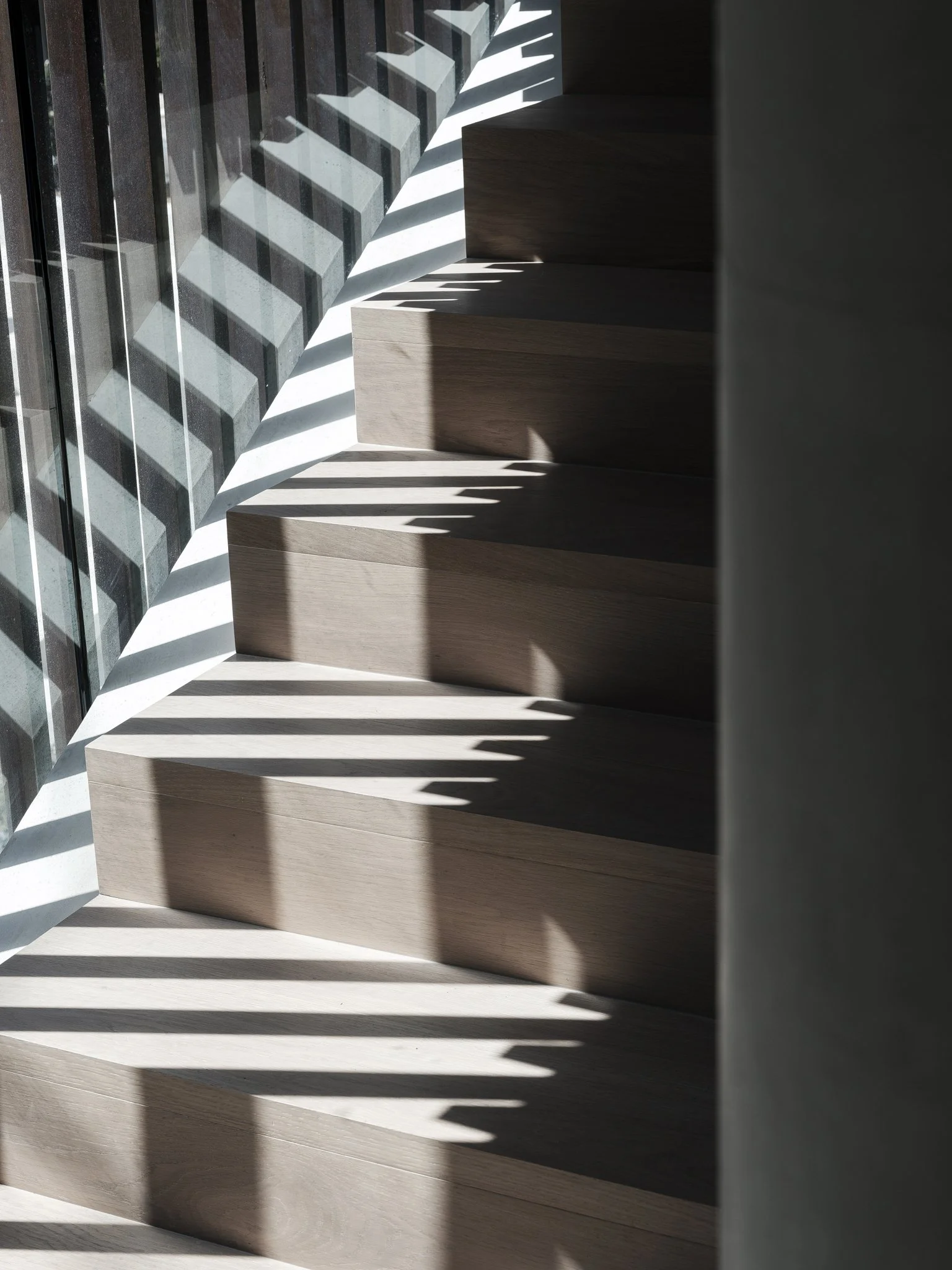A staircase with sunlight casting shadow patterns on the steps and adjacent glass wall with vertical metal bars.