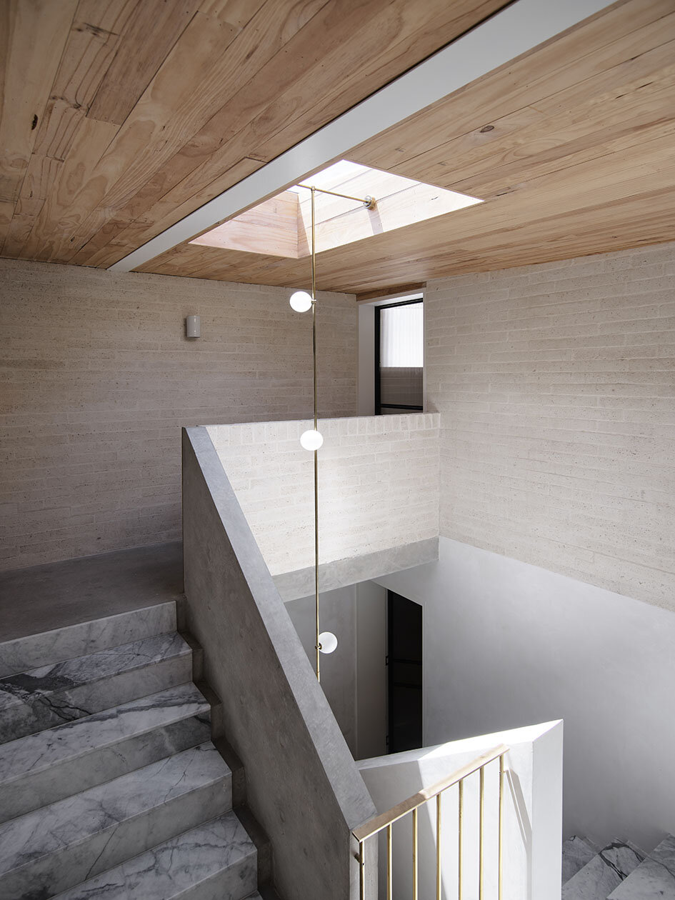 Interior of a modern home staircase with marble steps, concrete wall and railing, wooden ceiling with skylight, and a hanging light fixture.