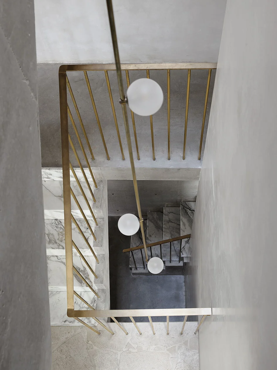 View looking down a staircase with gold railing and white spherical pendant lights hanging from the ceiling.