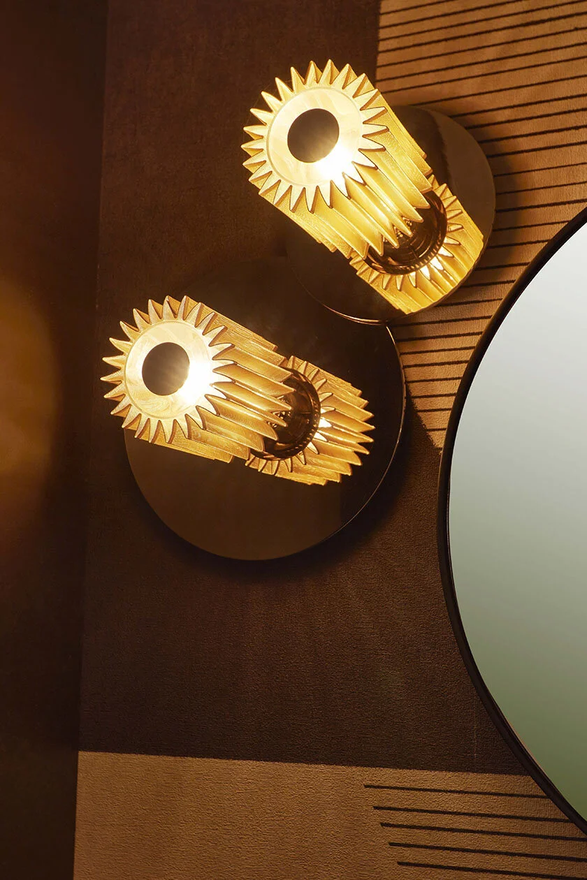 Close-up of two modern wooden wall sconces with circular lights, mounted on a textured wall near a curved mirror.