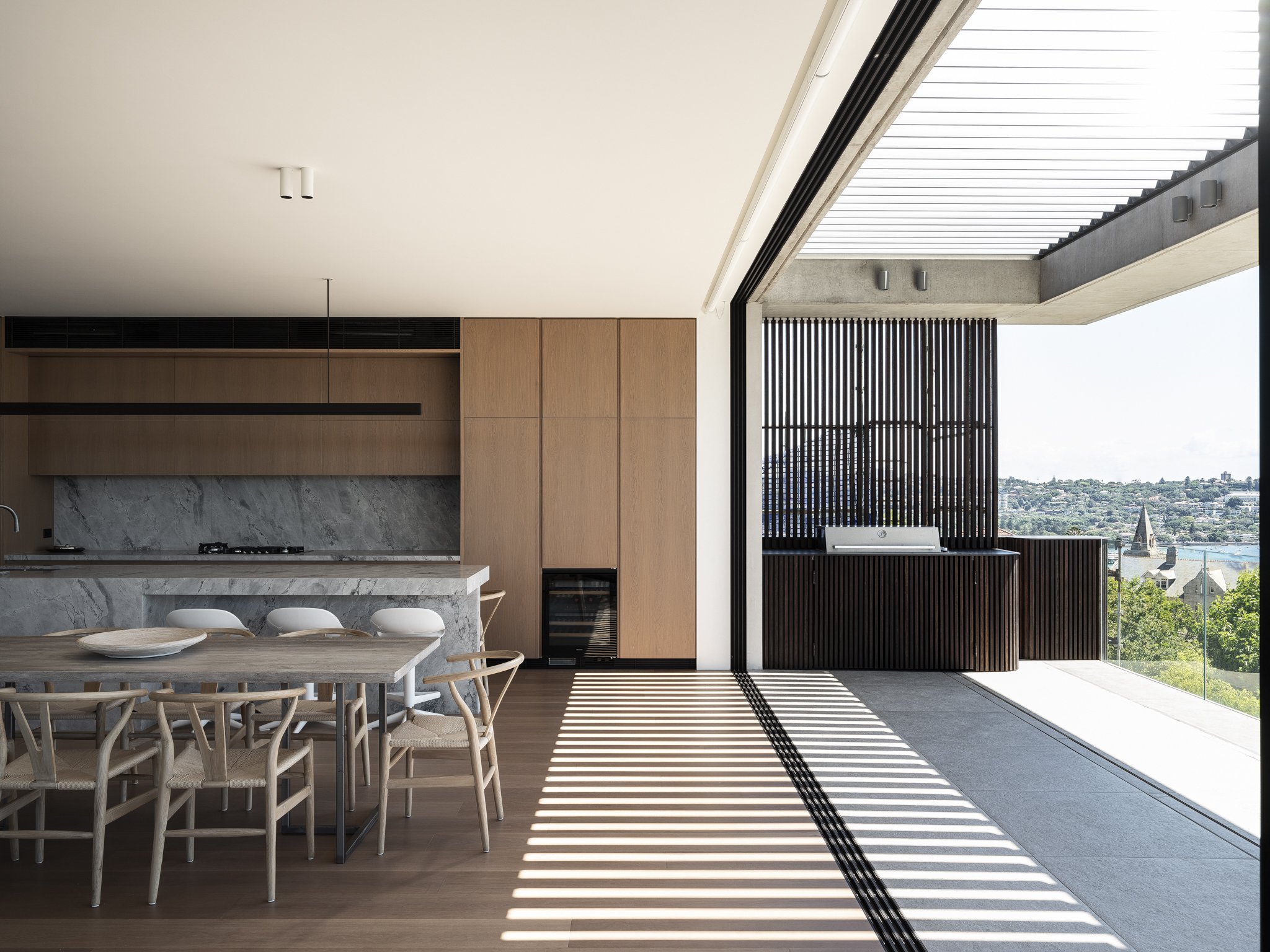 Modern kitchen and dining area with natural light, wooden furniture, marble countertops, and a view of a cityscape with a river and church steeples.