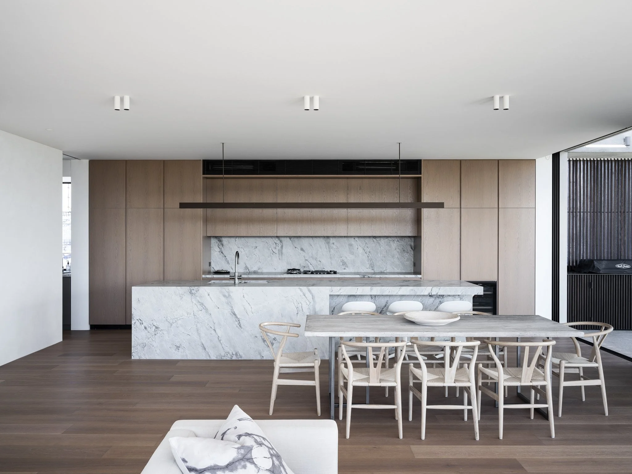 Modern open-plan kitchen with marble island, wooden cabinetry, and dining area with wooden chairs and a table