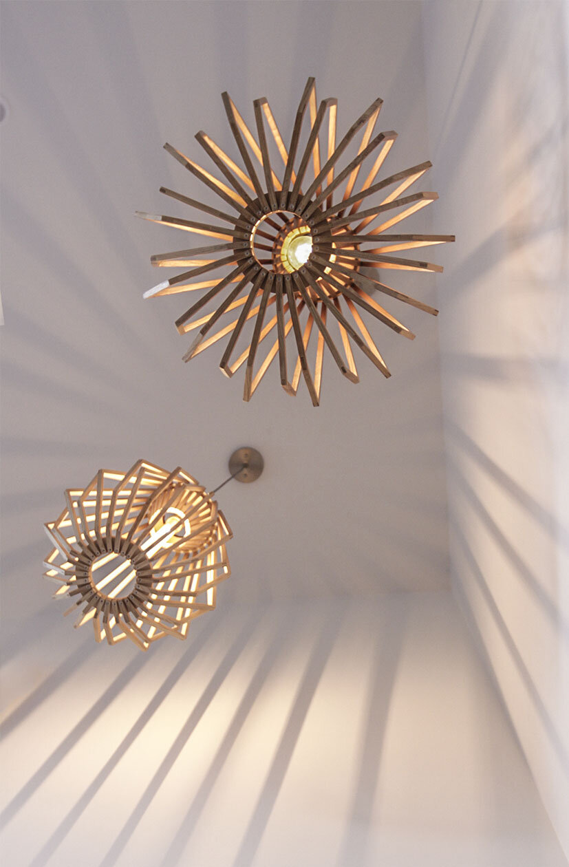 Two modern pendant lights with wooden slats casting shadows on the ceiling.
