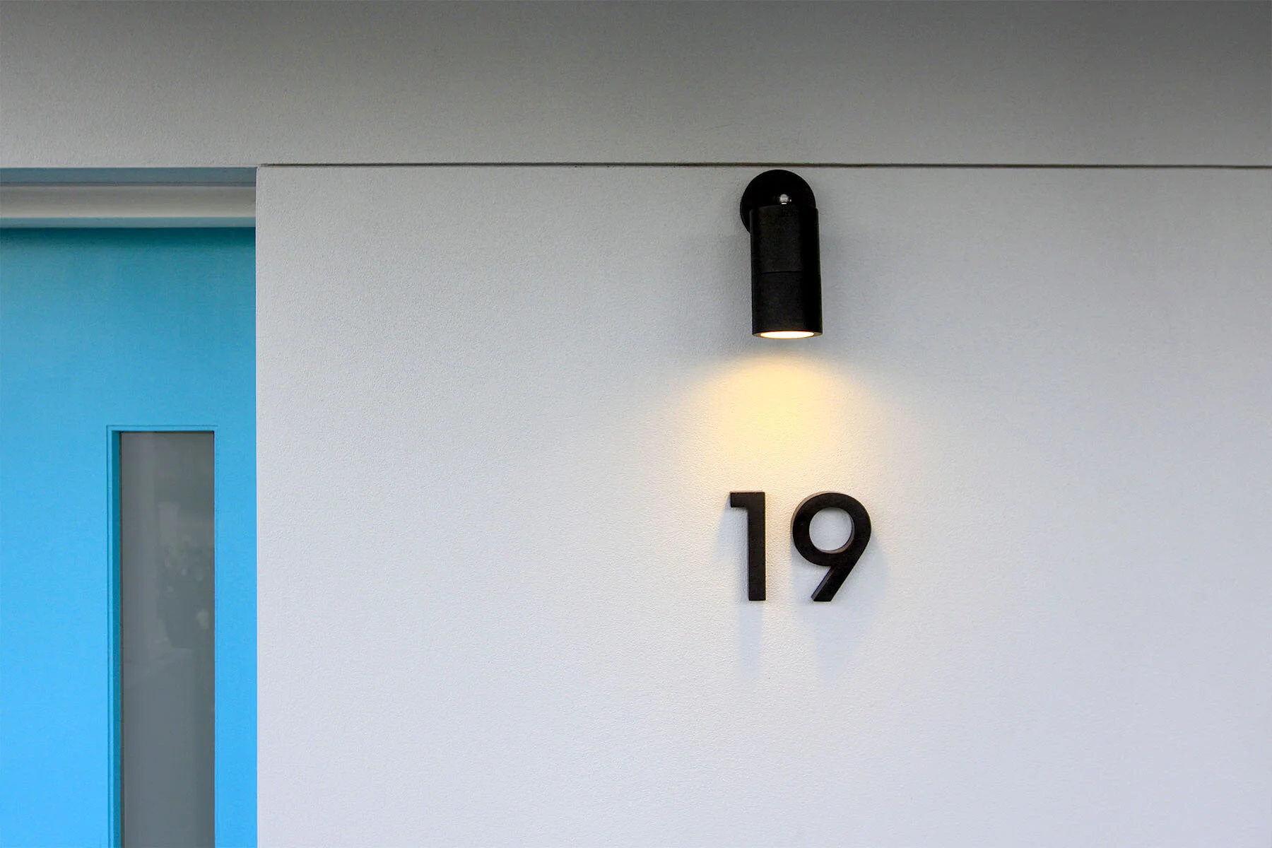 Wall with black number 19, black sconce light illuminating number, blue door frame on left