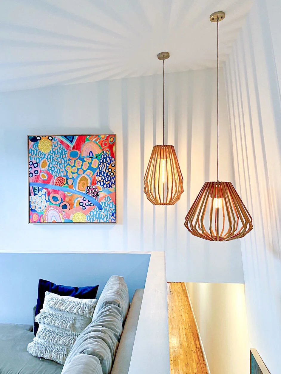 Interior of a modern home with two pendant lights, a colorful abstract painting on the wall, and a light-colored sofa with decorative pillows.