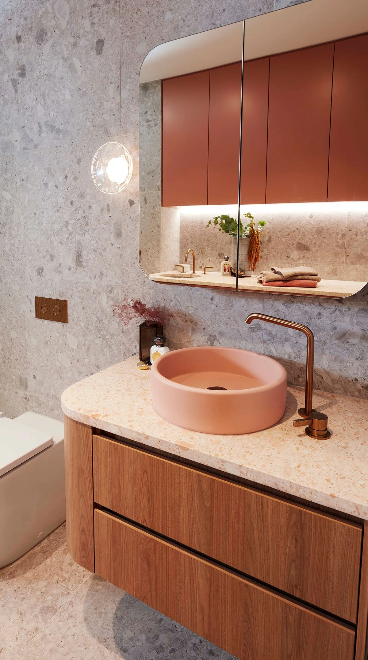 Modern bathroom with a pink sink, wooden vanity, marble countertops, a large mirror, and a bathroom mirror reflecting cabinetry.