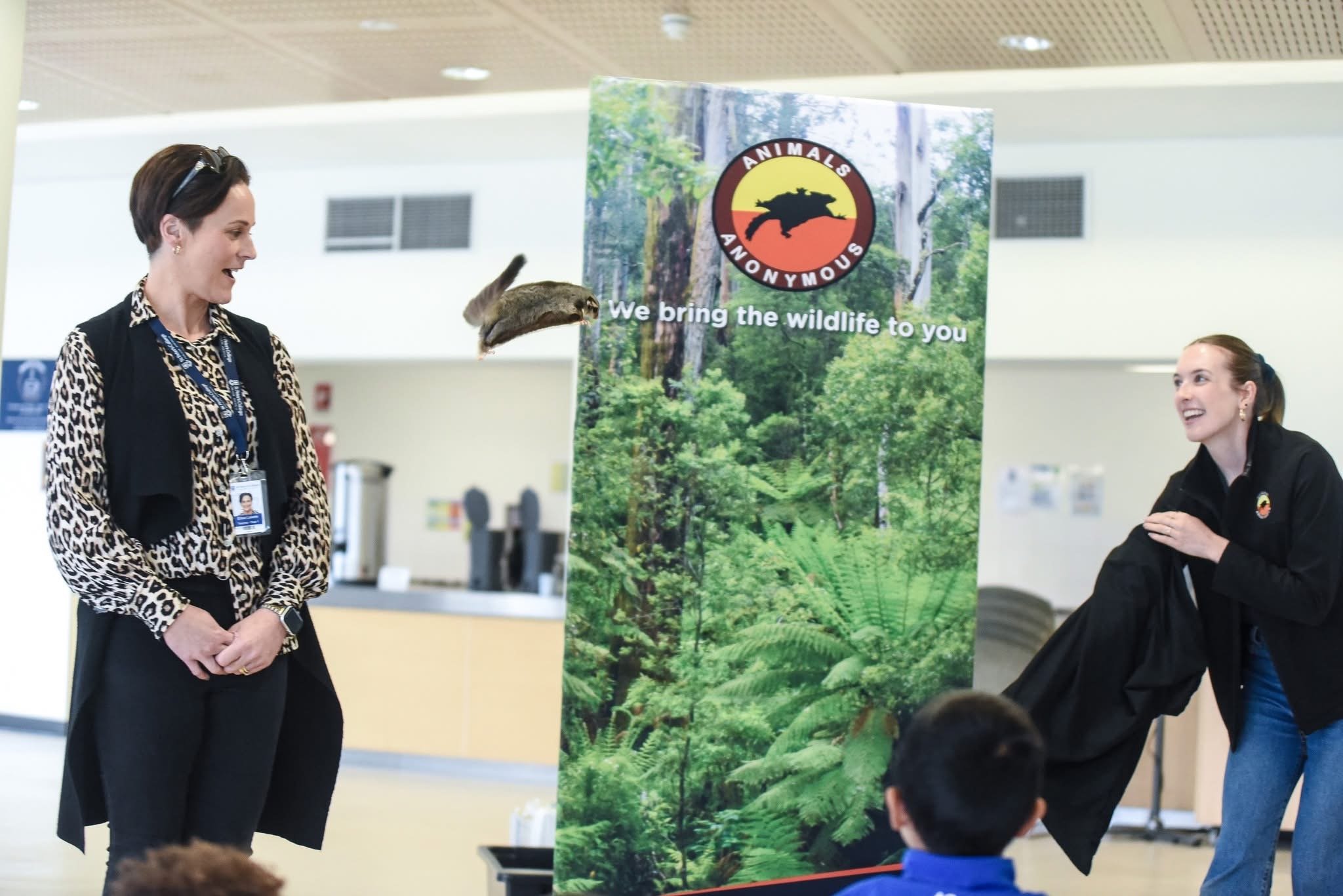 Two women at a wildlife demonstration. A squirrel glider has jumped and is gliding between them.