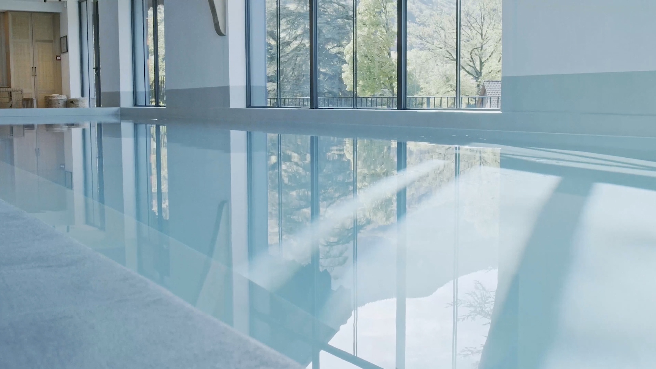 Indoor swimming pool with large windows letting in natural light and views of trees outside.