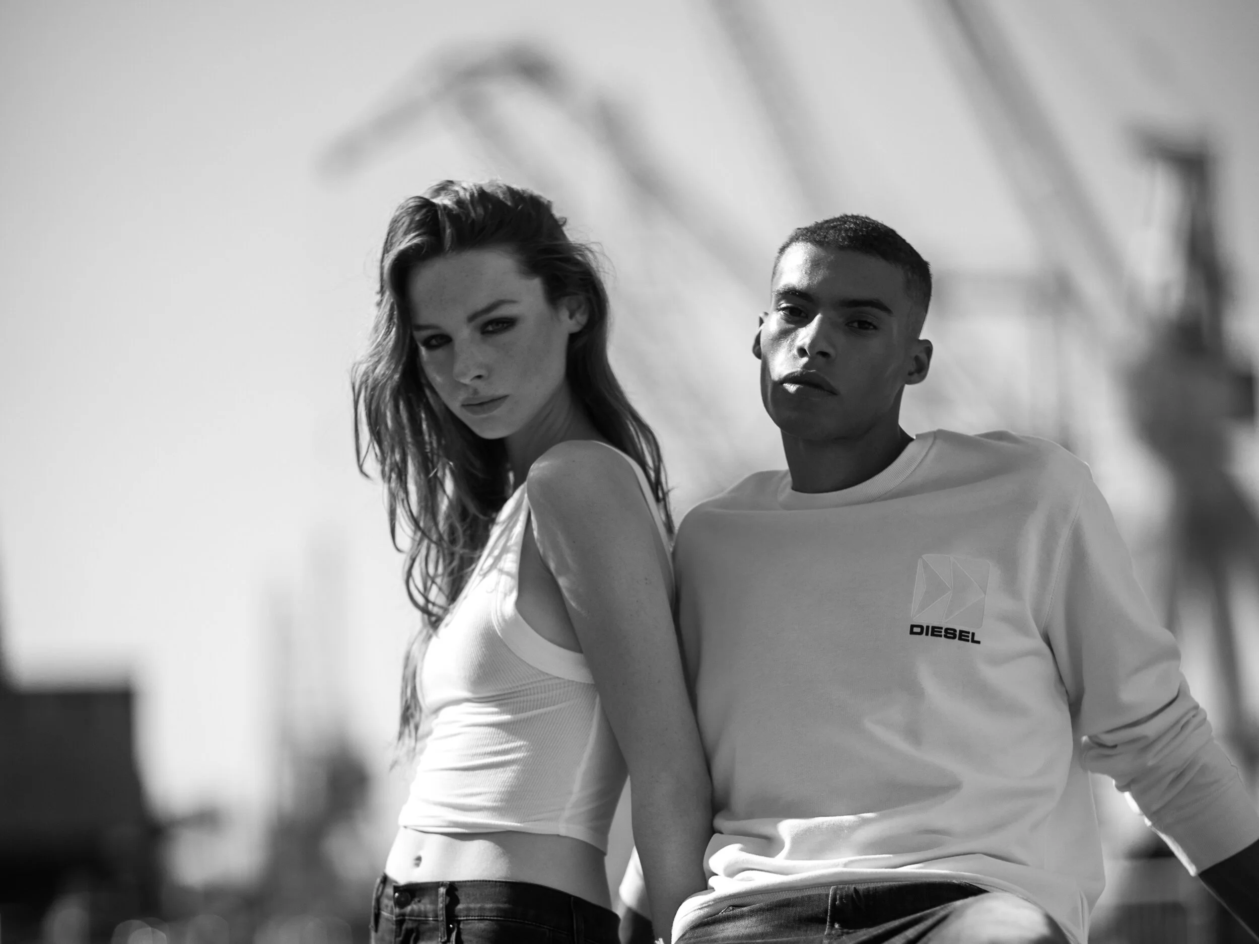 Black and white photo of a young woman and man posing outdoors, with the woman standing slightly behind and to the left of the man, both looking at the camera with serious expressions.