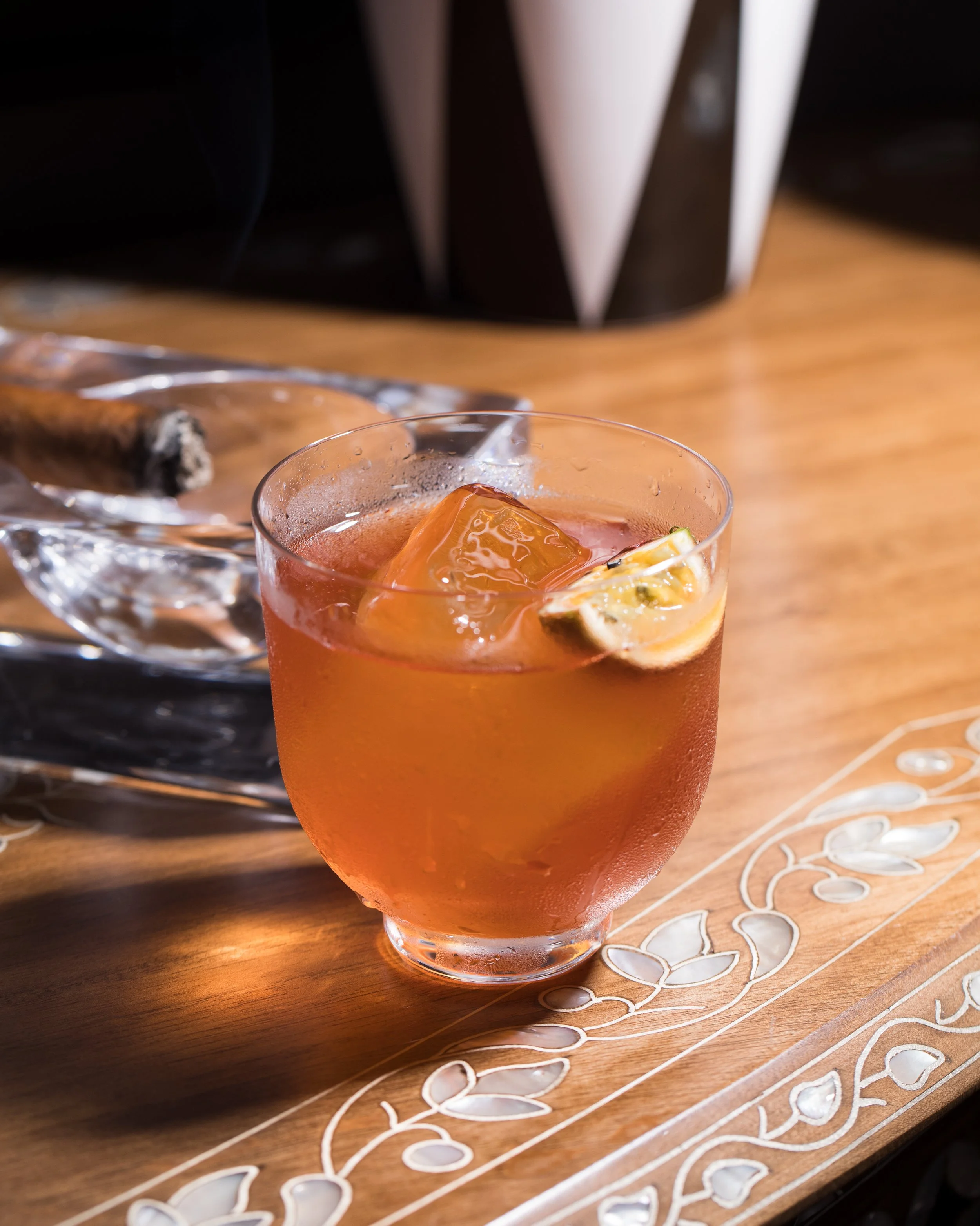 A glass of iced tea with lemon slice on a wooden table with decorative white floral patterns.