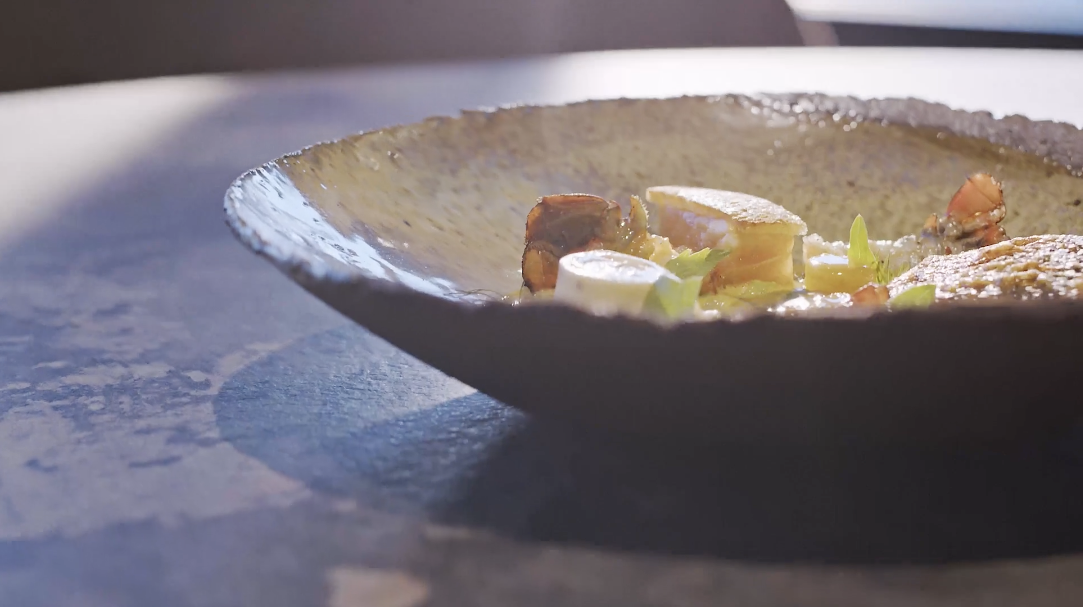 Close-up of a ceramic bowl with cooked vegetables and chunks of meat, placed on a dark wooden surface.