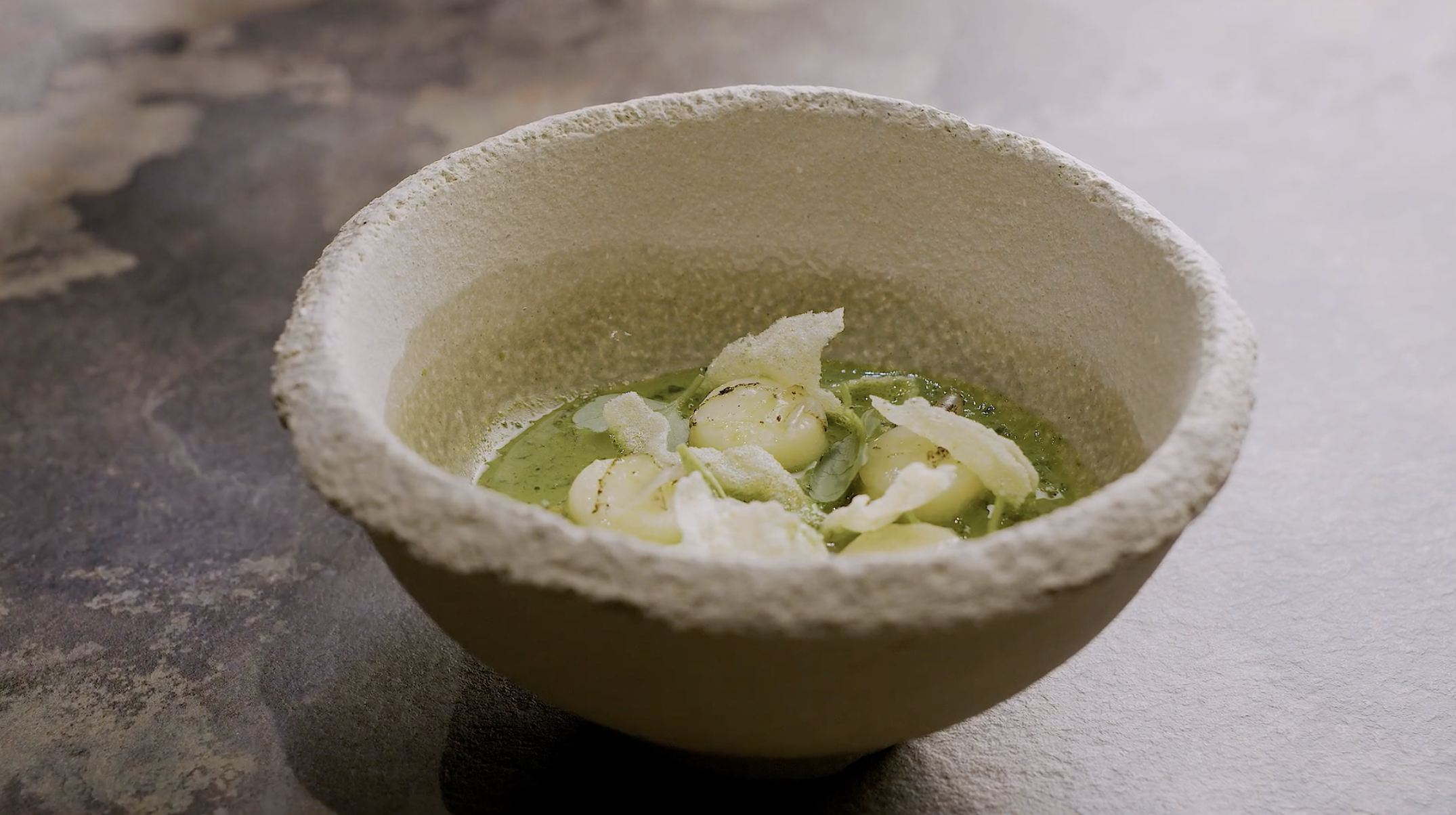 A bowl of green soup garnished with small white cheese balls and crispy cheese wafers.