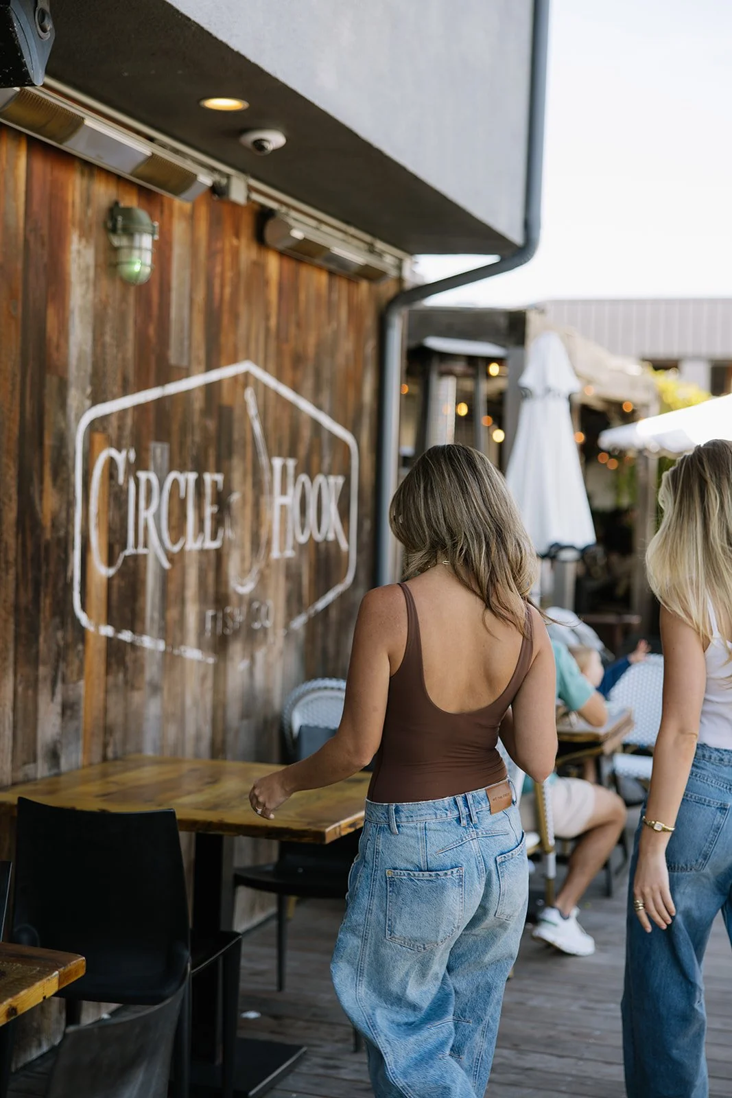 Women standing outside Circle Hook restaurant, wooden wall with logo, and other patrons seated in the background.