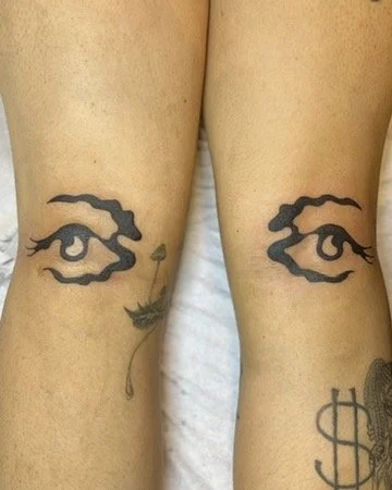Tattooed eyes and a dangling earring on a person's legs.