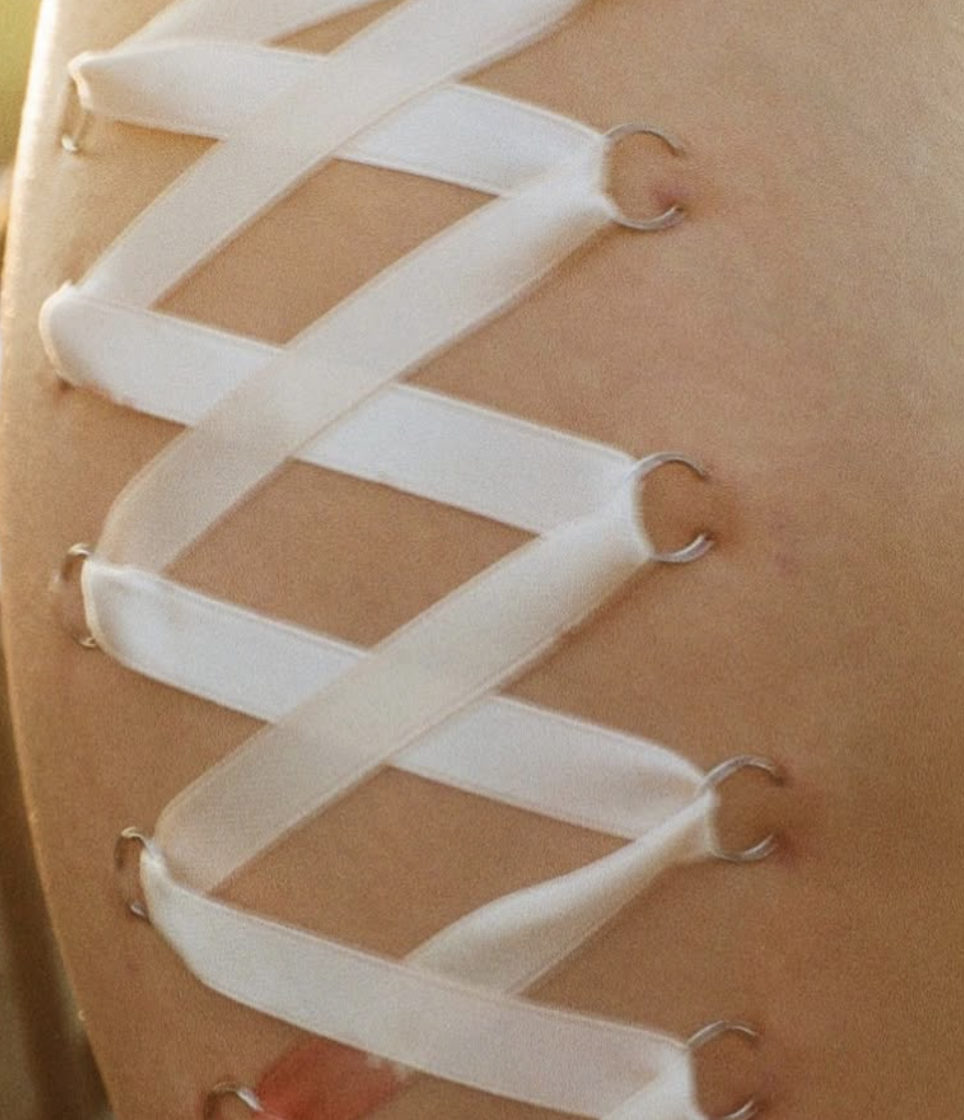 A close-up of a person’s back showing white elastic straps with metal hooks attached to skin, likely as part of a medical or sports accessory.