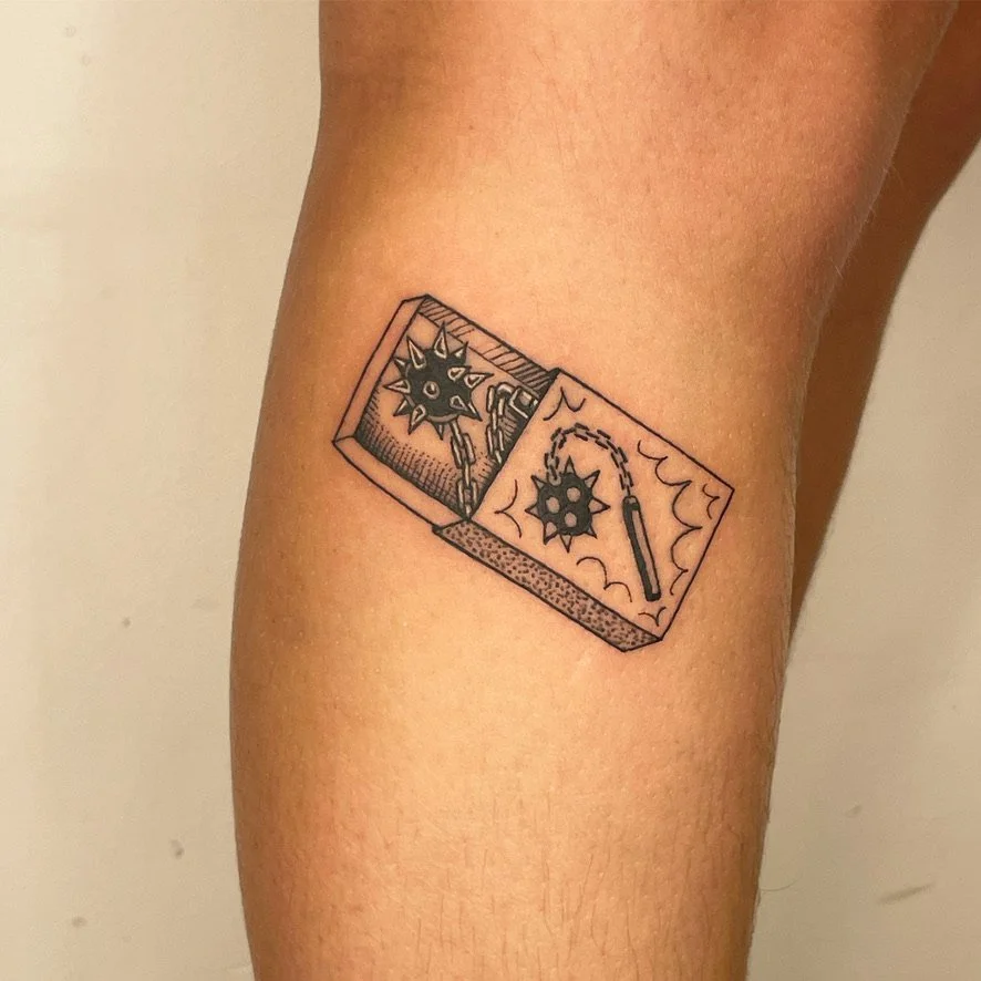 Tattoo of a mousetrap with a spiky ball, on a person's upper thigh.
