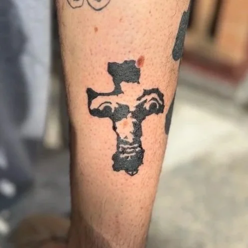 Tattoo on person's arm resembling a distorted face with dark ink.