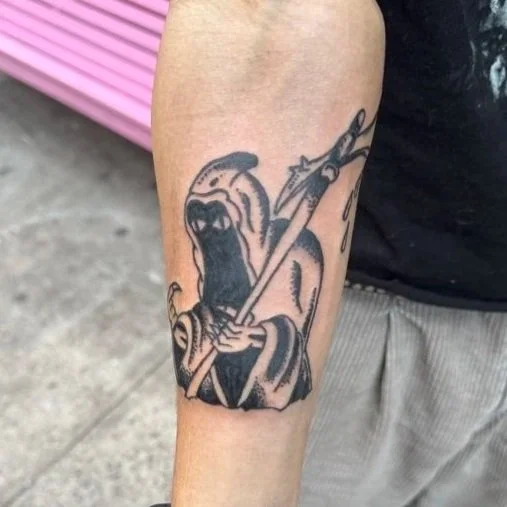 Tattoo of a Grim Reaper holding a scythe on a person's forearm.