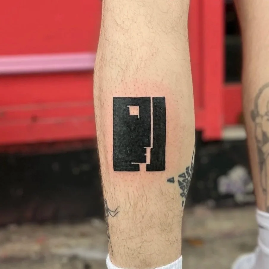 Black geometric tattoo on person's lower leg with a red background.