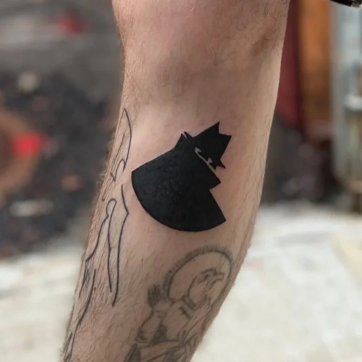 A person's arm with a black silhouette tattoo of a cat wearing a crown, partially covering some sketches or drawings underneath.