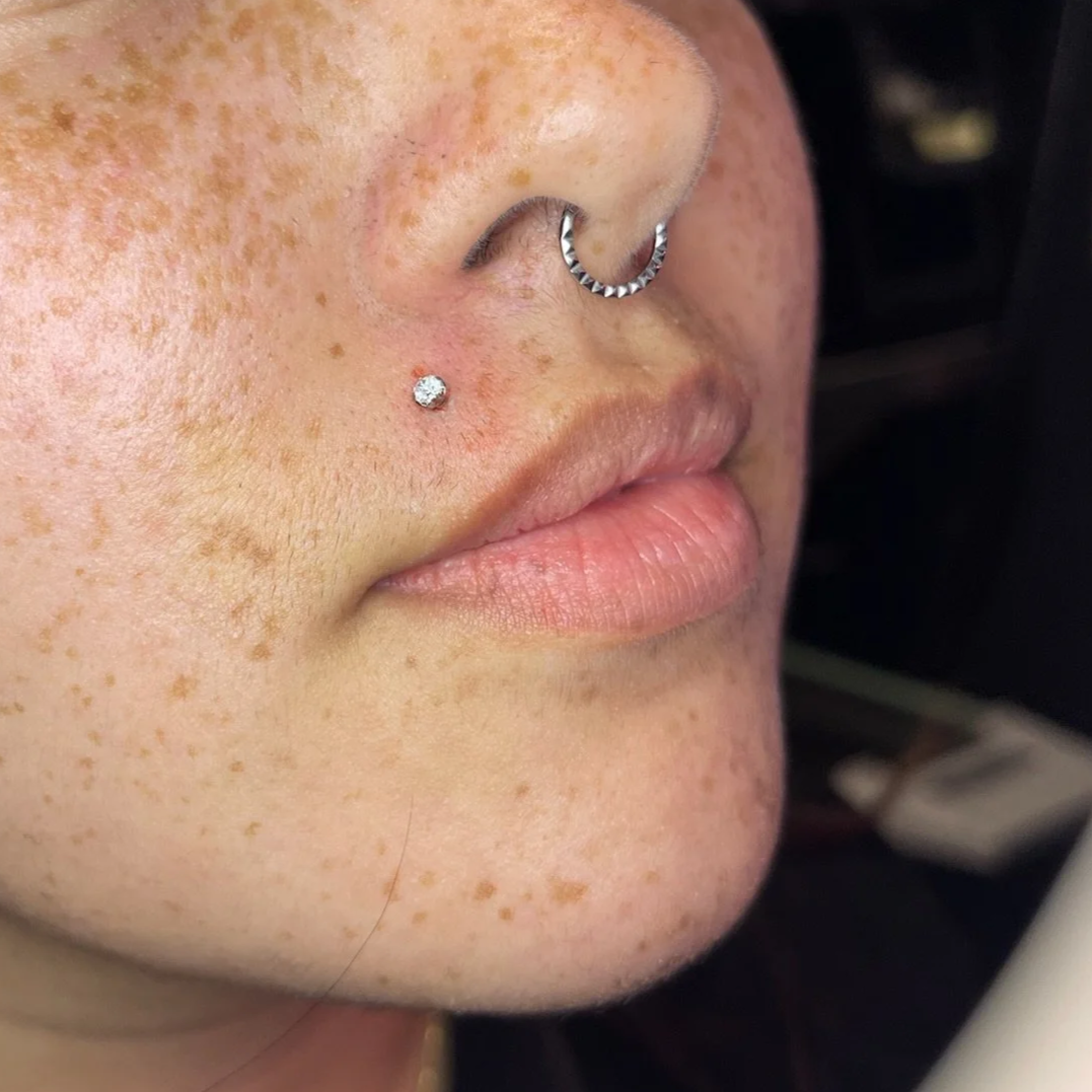 Close-up of a person's face with freckles, featuring a nose piercing and a small diamond stud.