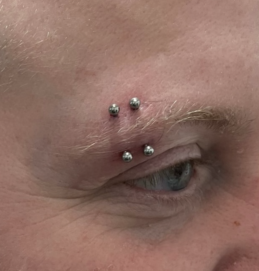 Close-up of a person's face showing a pierced eyebrow with four metal studs.