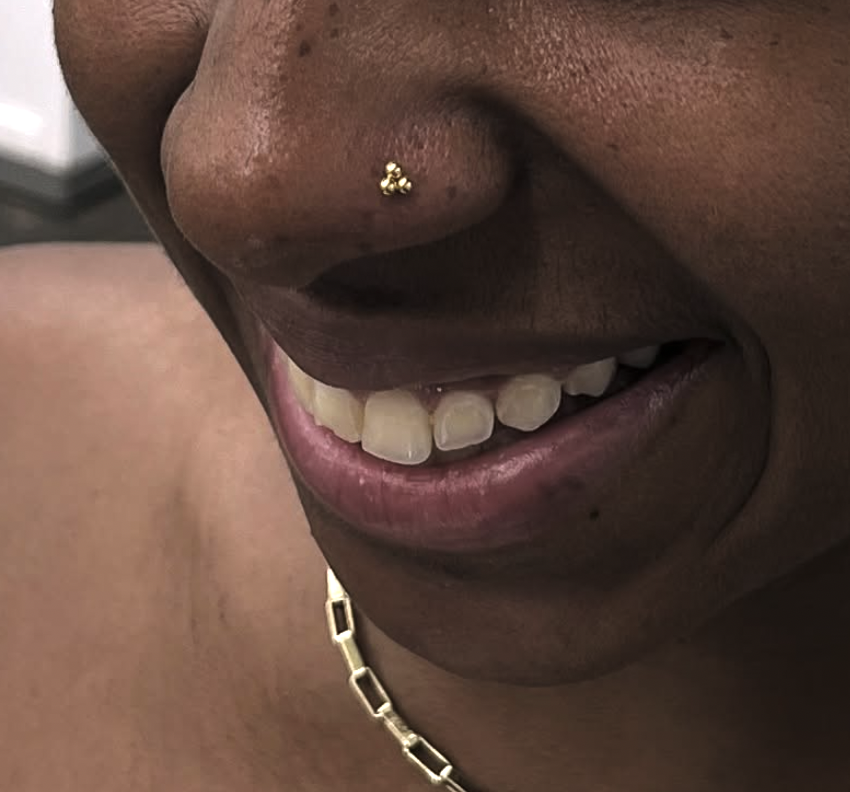 Close-up of a smiling person with a gold nose stud and wearing a gold chain necklace.