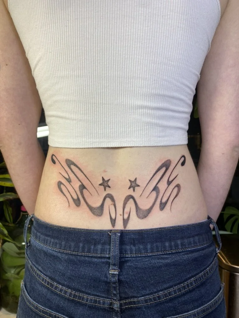 Tattoo of abstract wings and two stars on a person's lower waist.