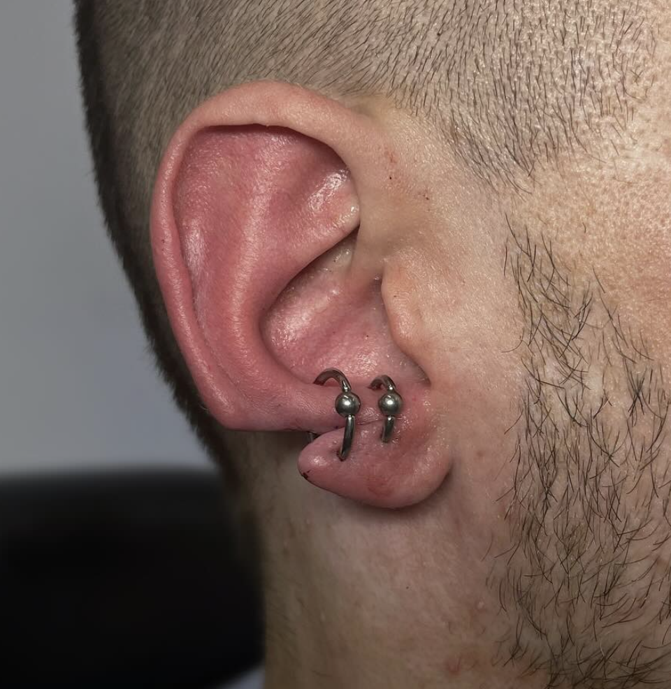 Close-up of a person's ear with two small hoop earrings, one in the helix and one in the earlobe.